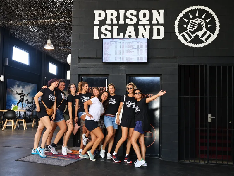 Um grupo de amigos com t-shirts iguais posa em frente ao letreiro da Prison Island